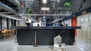A modern reception area with a 'CHECK-IN' sign, a guitar, and a 'SAY HELLO TO MOXY' sign. - Moxy Pompeii (Torre Annunziata)