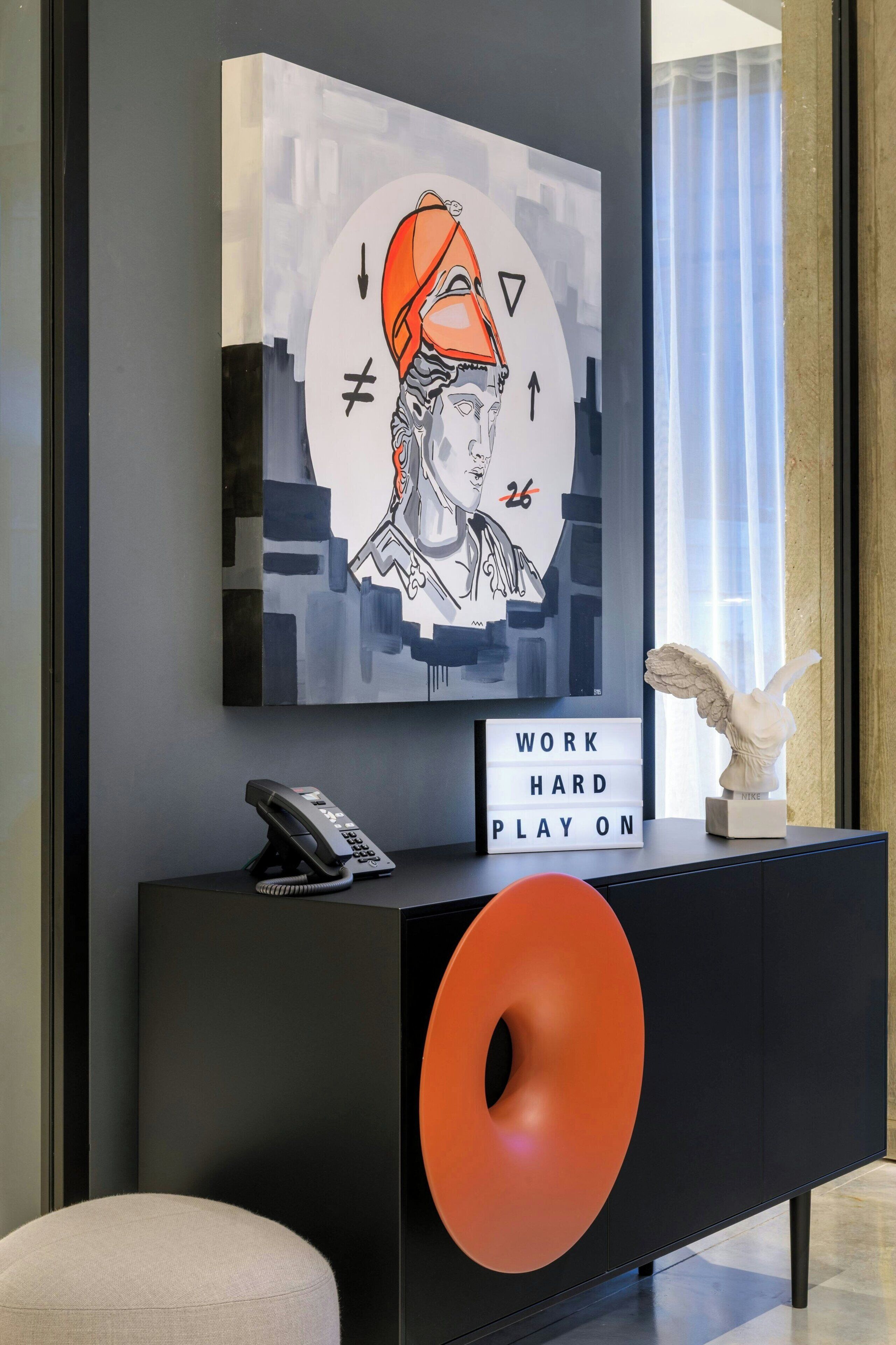 A modern interior with a large abstract painting, a motivational sign, a sculpture, and a telephone on a black console.