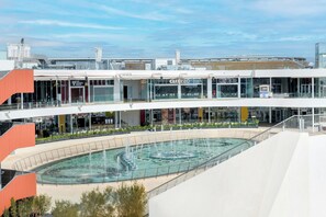 Ein mehrgeschossiges Einkaufszentrum mit einer zentralen Fontäne, Glasfassaden und modernem Architekturstil.