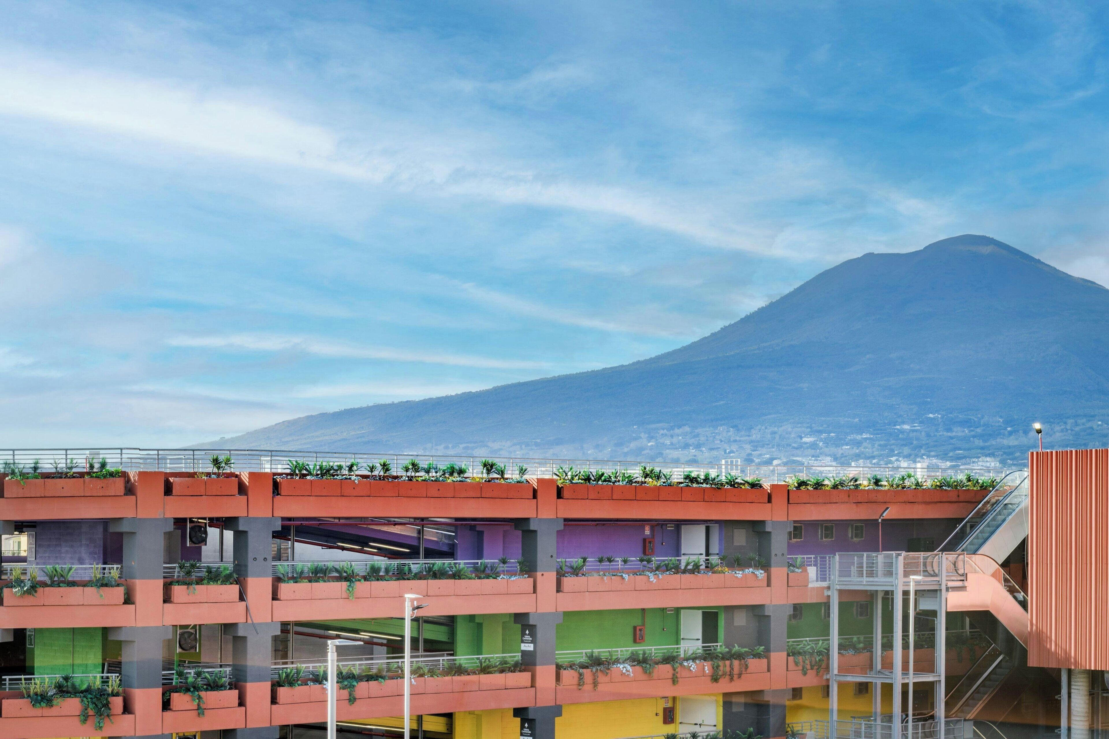 A multi-story building with balconies, a staircase, and a view of a mountain.
