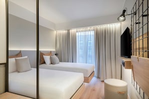 A modern hotel room with two beds, a TV, a mirror, and a window with curtains. - Moxy Pompeii (Torre Annunziata)