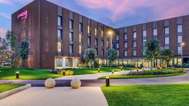 A modern hotel with a prominent neon sign, a well-maintained garden, and a clean, contemporary design. - Moxy Pompeii (Torre Annunziata)