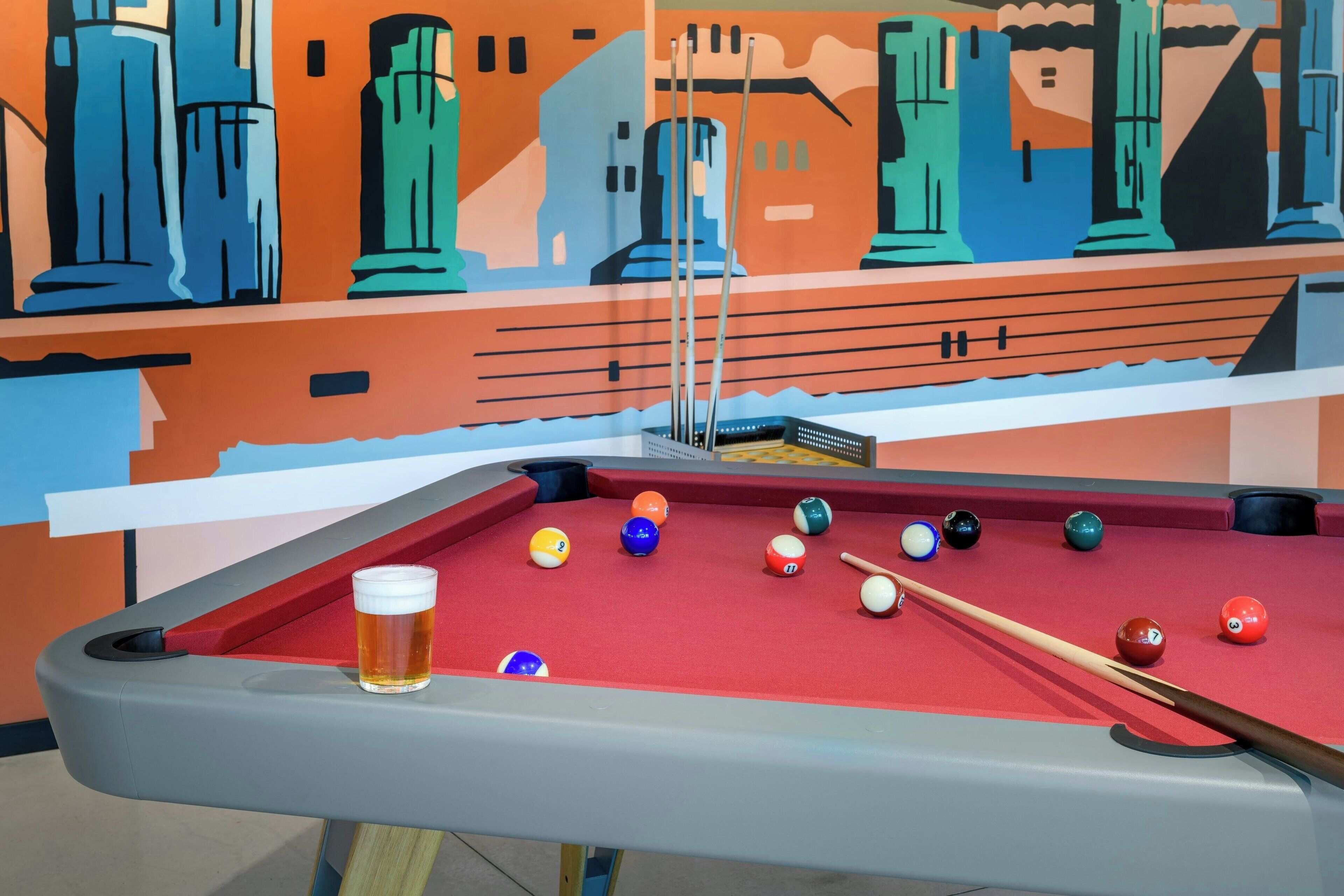 A pool table with a glass of beer, pool balls, and a pool cue.
