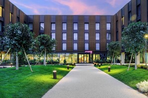 A modern hotel with a central entrance, surrounded by well-maintained greenery and a pathway leading to the entrance. - Moxy Pompeii (Torre Annunziata)