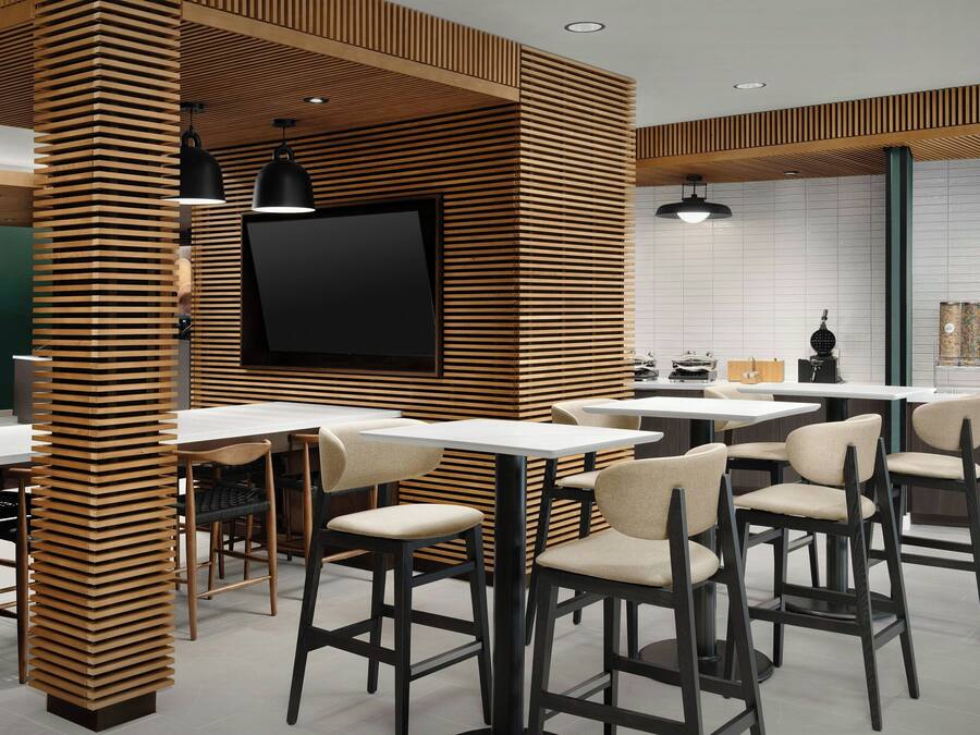 A modern restaurant interior with wooden slat partitions, black pendant lighting, and a flat-screen TV mounted on the wall.