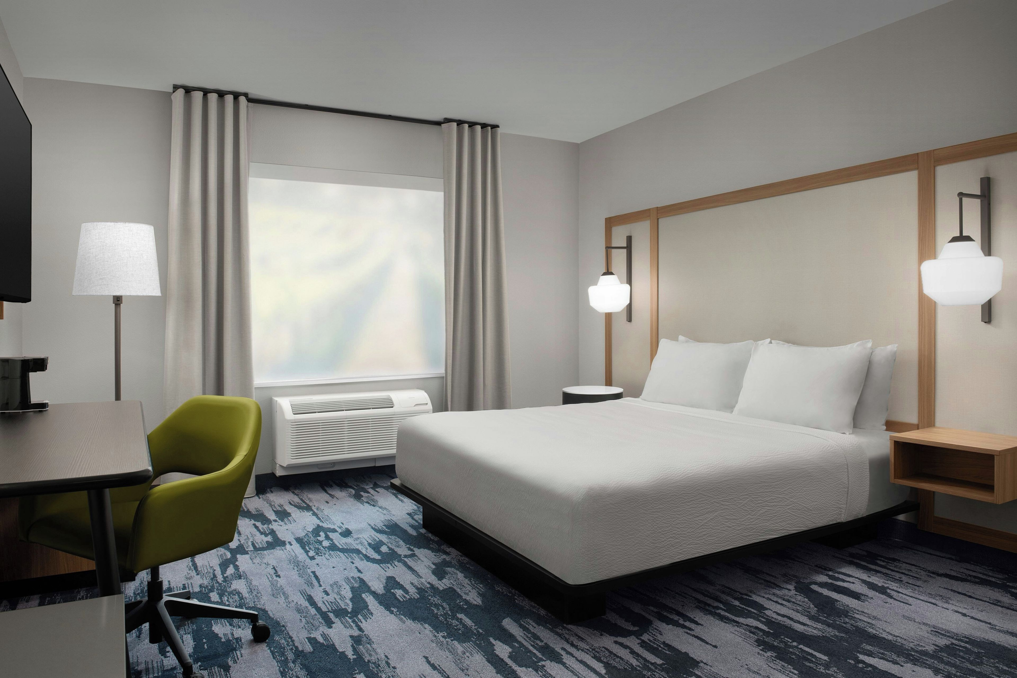 A hotel room with a bed, a desk, a chair, a TV, and a window with curtains.