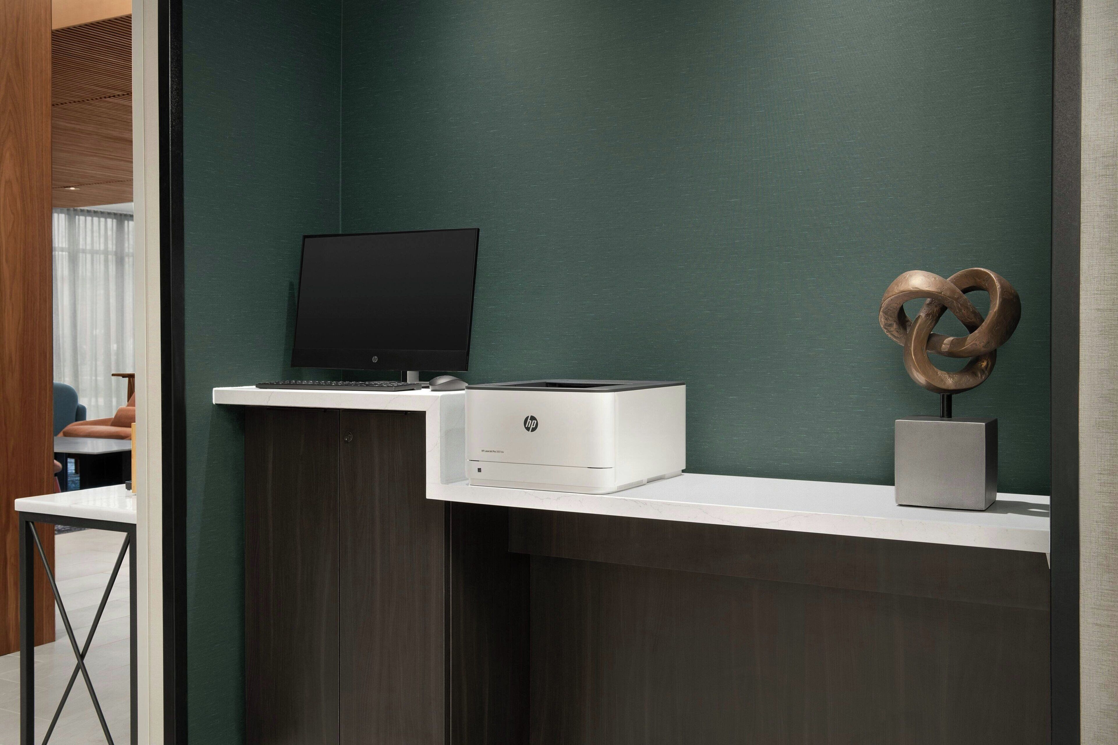 A modern office desk with a laptop, HP printer, and decorative sculpture.