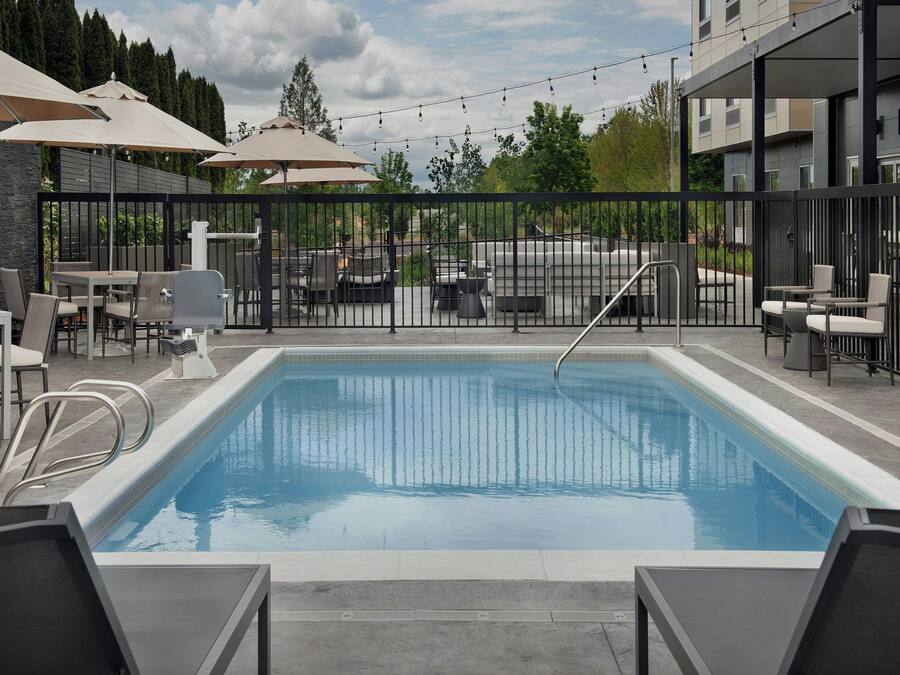 A swimming pool with lounge chairs and umbrellas, surrounded by a fence and outdoor furniture.