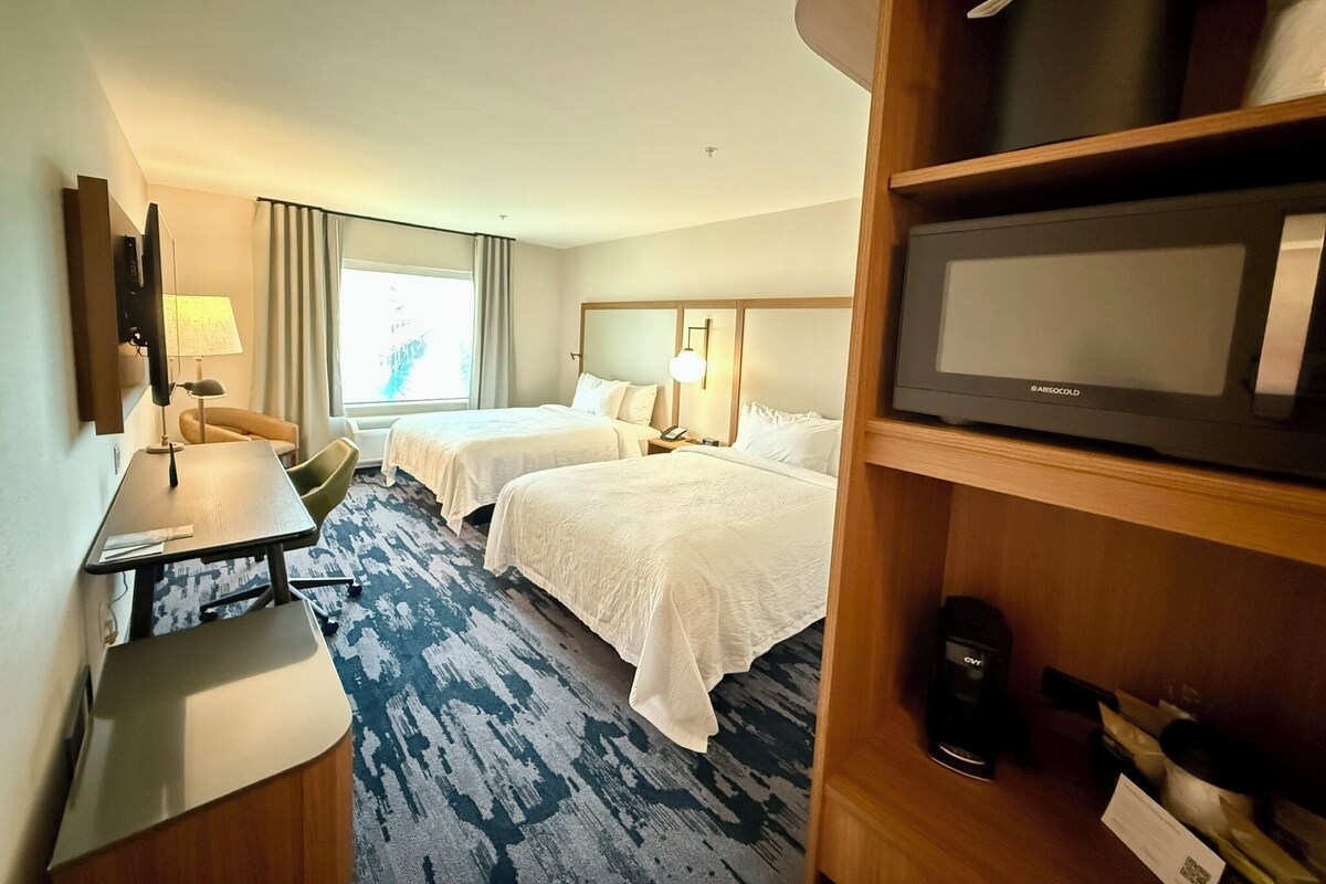 A hotel room with two beds, a desk, a TV, and a minibar.