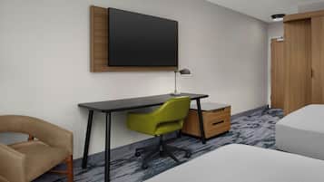 Een hotelkamer met een bureau, een groene bureaustoel, een bed, een garderobe en een wandgemonteerde flatscreen-tv.