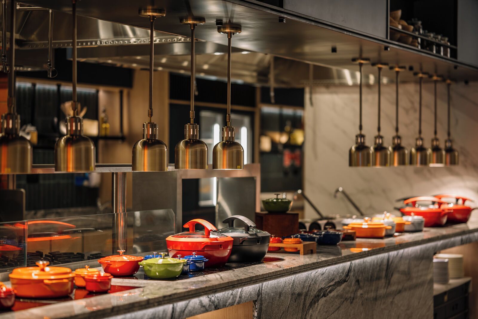 A kitchen with stainless steel appliances, hanging pendant lights, and colorful cookware on the counter.