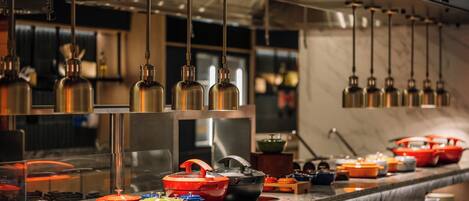 A kitchen with stainless steel appliances, hanging pendant lights, and colorful cookware on the counter.