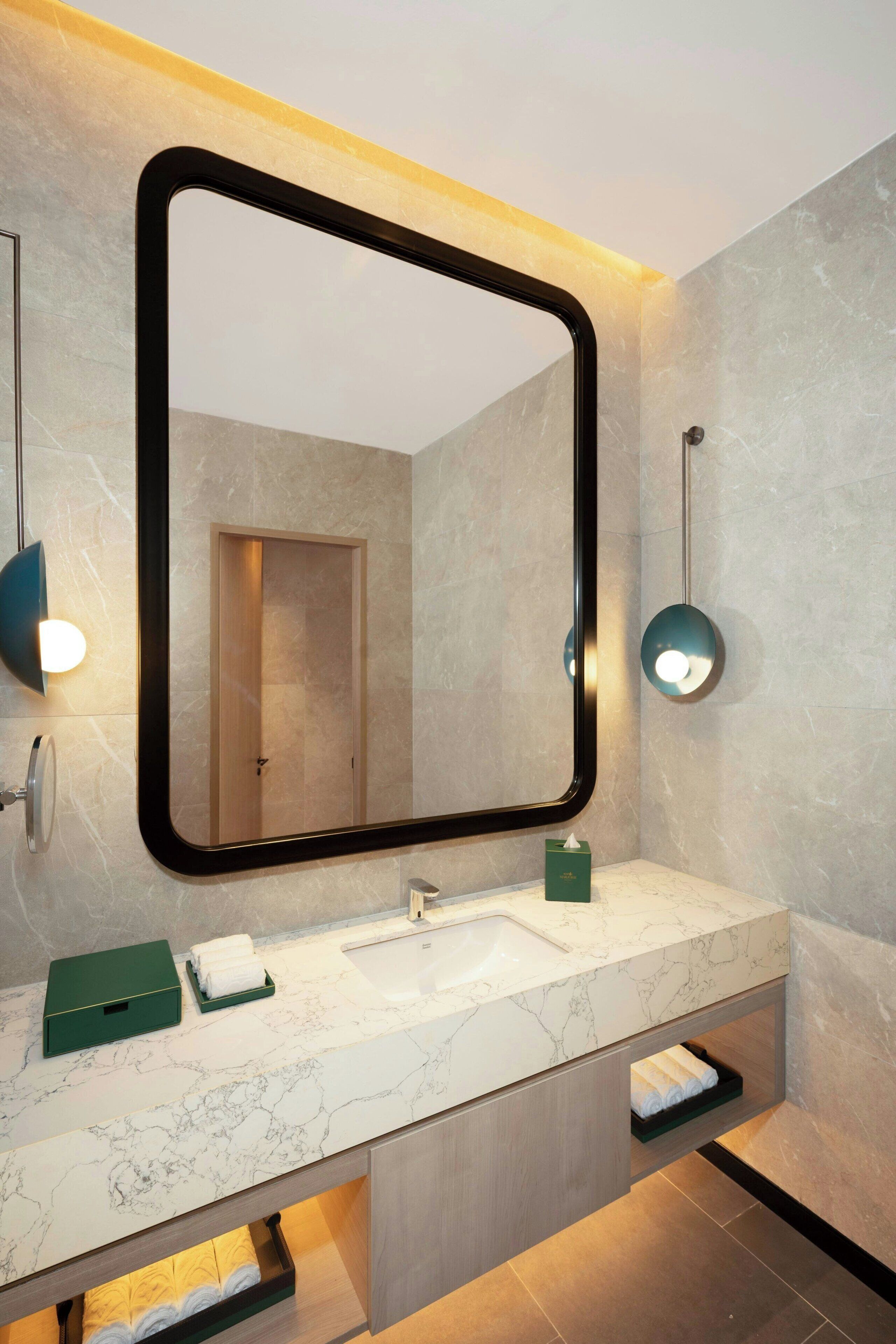 Un baño moderno con un espejo grande, encimera de mármol y estantes empotrados.