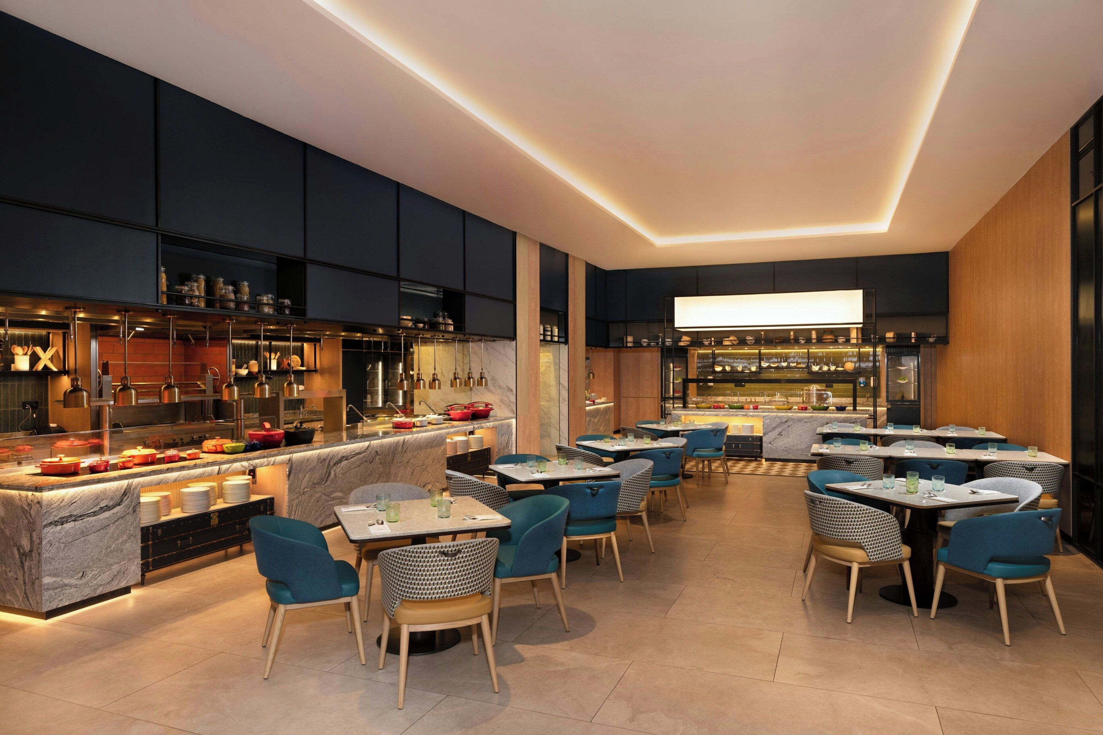 Un restaurant moderne doté d’un bar, de comptoirs en marbre et de chaises recouvertes d’un tissu bleu.