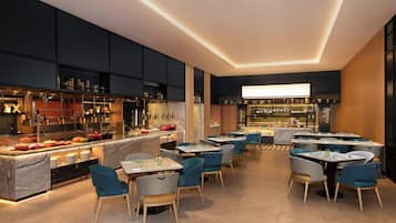 Moderni ravintola, jossa on baarialue, marmoritasot ja sinisellä kankaalla verhoillut tuolit.