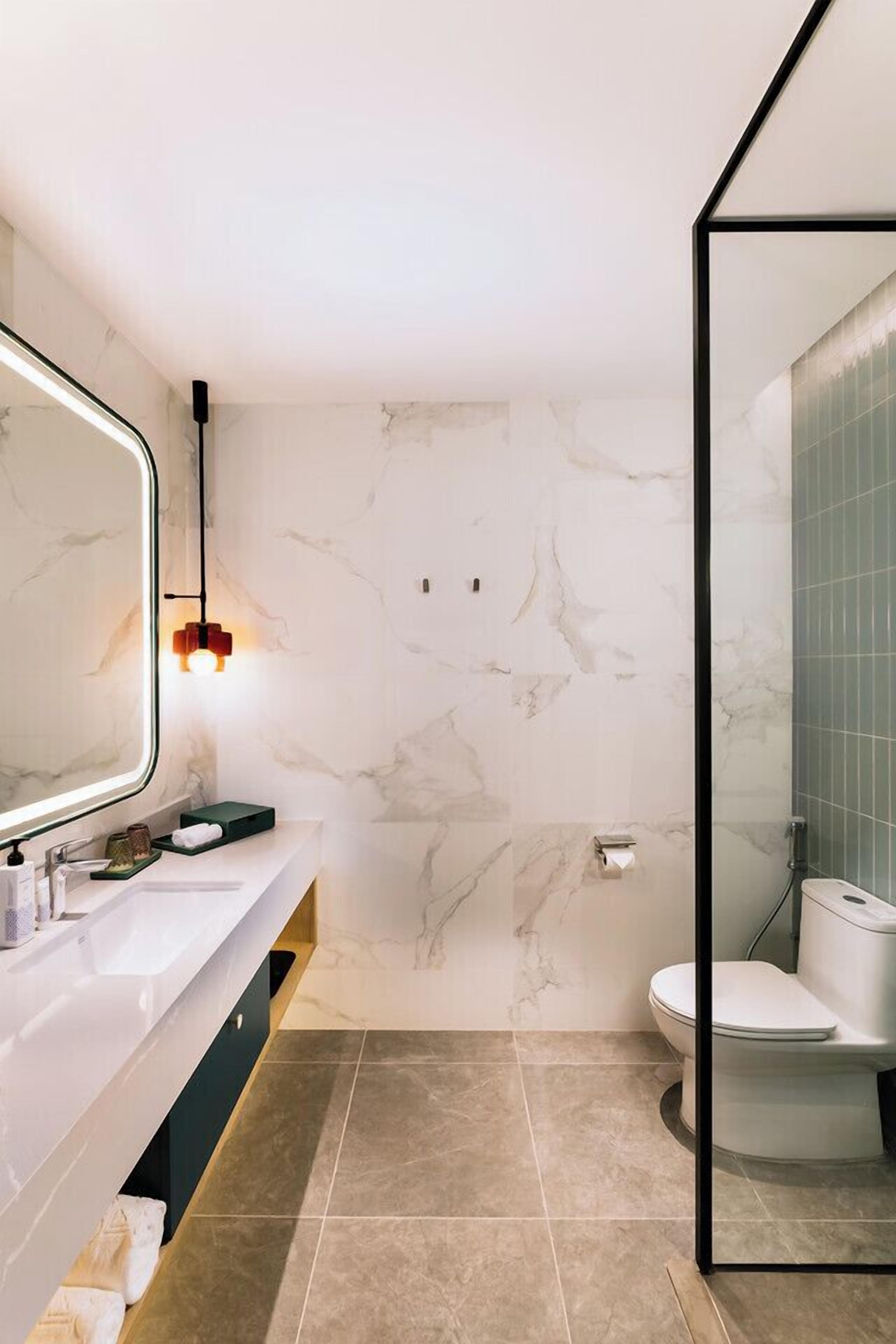 A modern bathroom with a marble wall, a glass shower enclosure, and a white sink with a mirror.