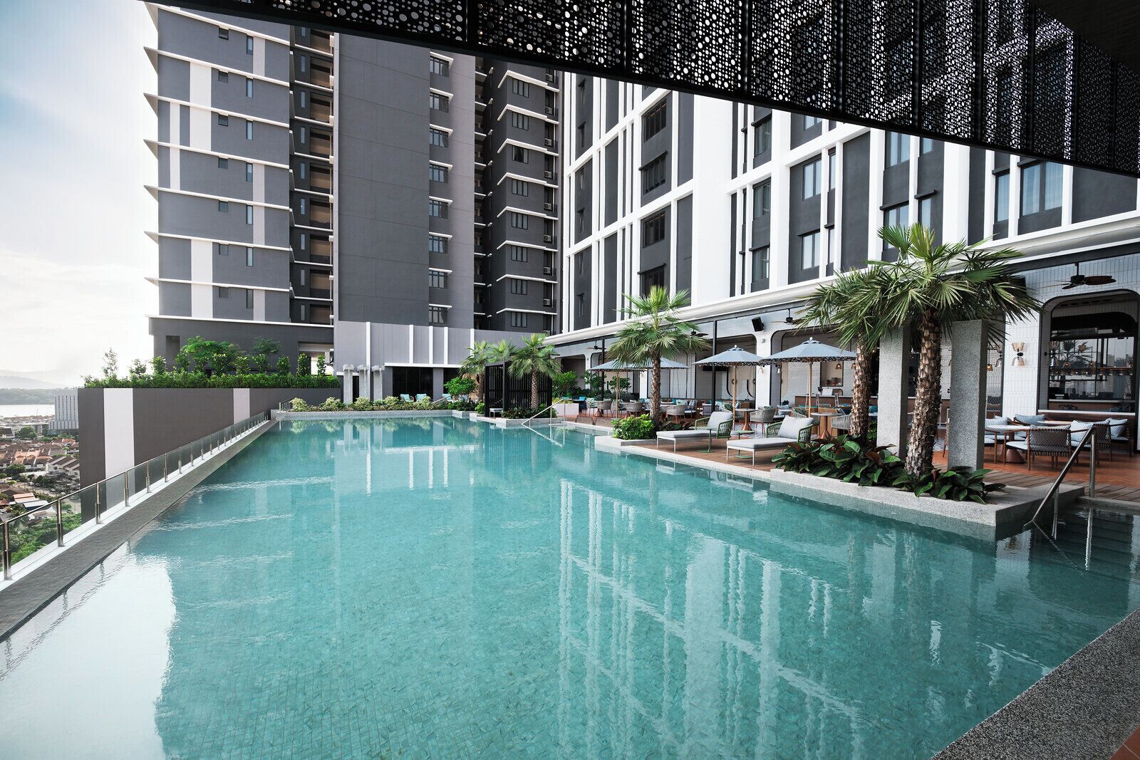 A rooftop pool with lounge chairs and umbrellas, surrounded by a modern building with balconies.