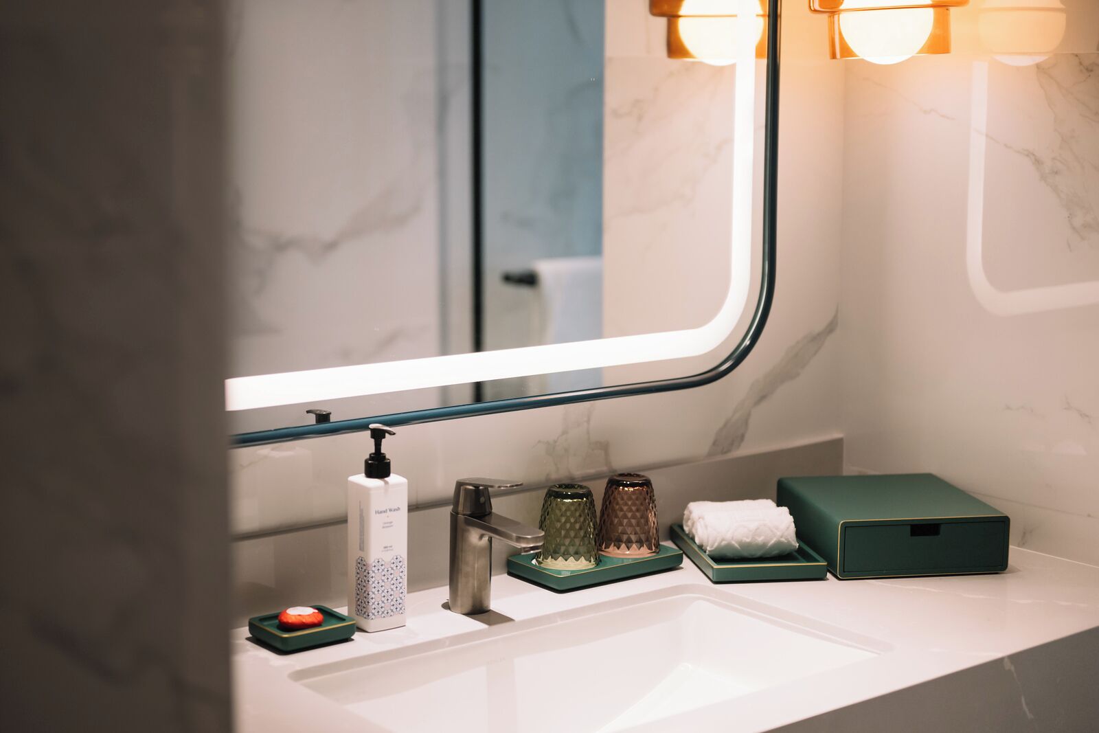 A modern bathroom with a white sink, a hand soap dispenser, a razor, and a green soap dish.