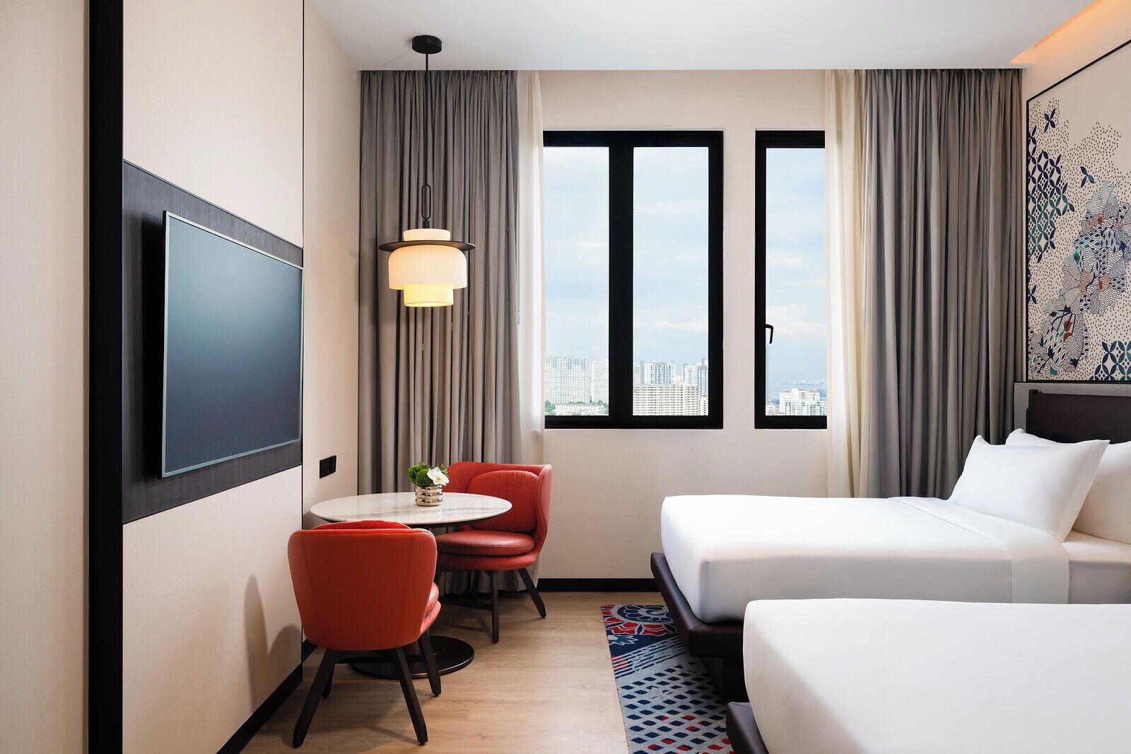 A hotel room with a bed, a desk with a chair, a TV, and a window with a city view.