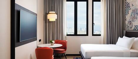 A hotel room with a bed, a desk with a chair, a TV, and a window with a city view.