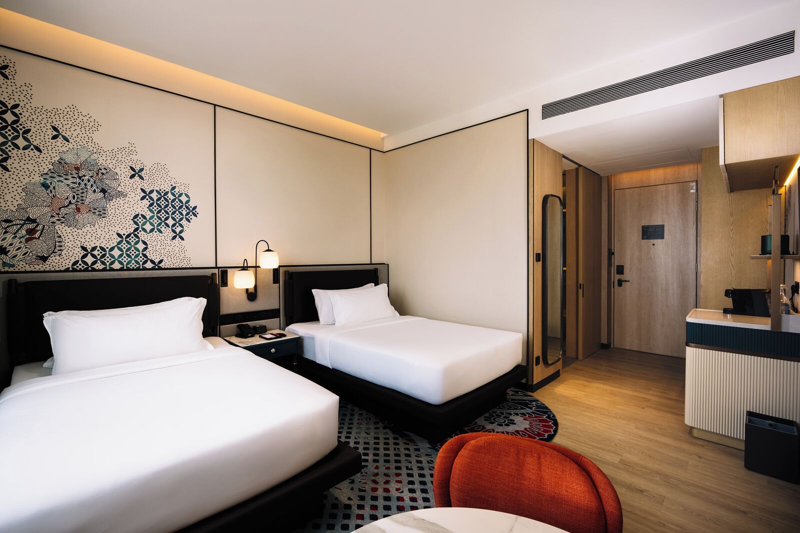 A hotel room with two beds, a desk, a chair, and a bathroom.