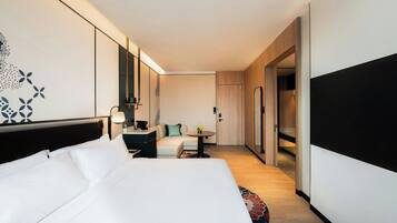 A modern hotel room with a large bed, a sofa, a small table, and a desk. There is a door leading to a bathroom and a closet.