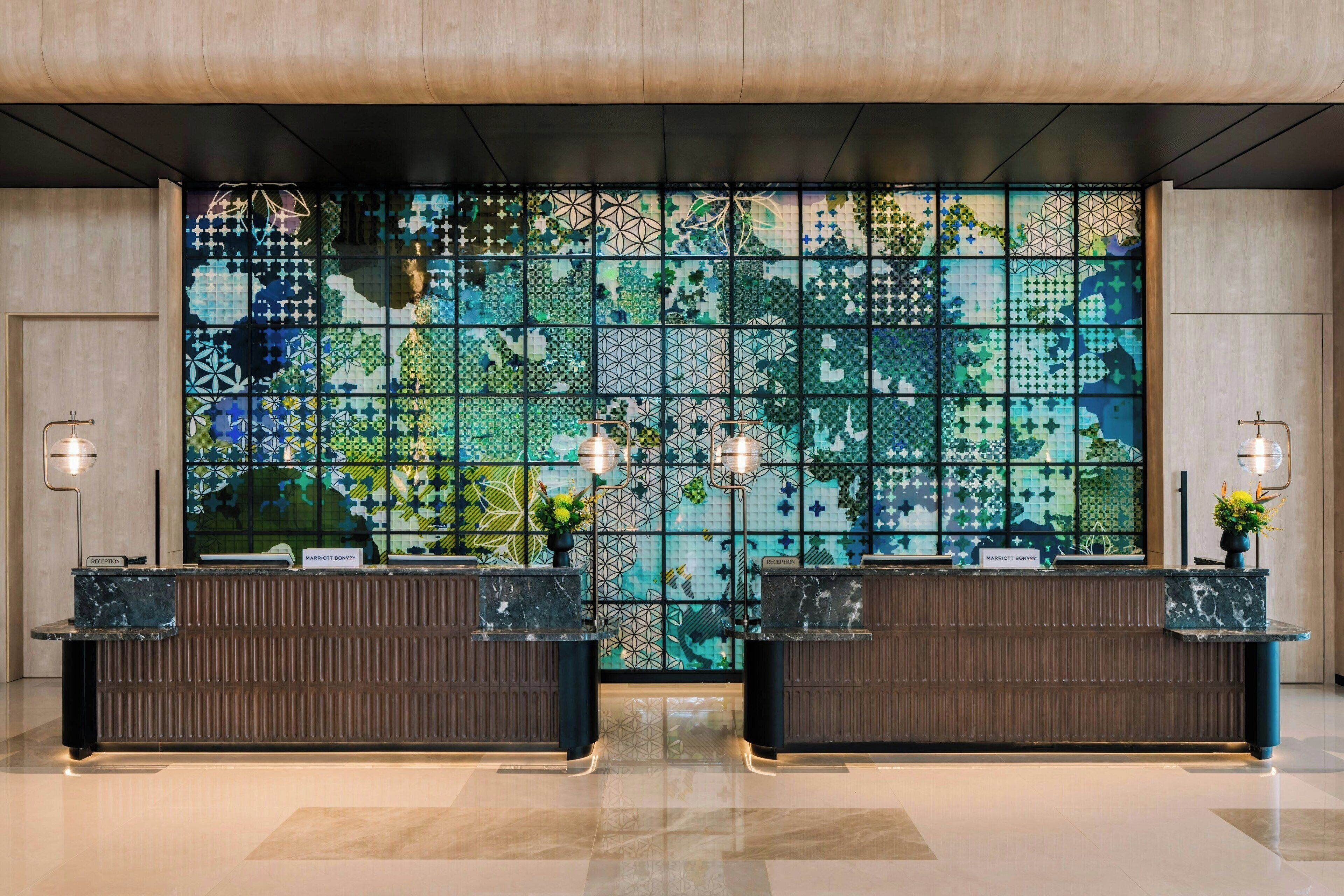 Un hall d’accueil d’hôtel agrémenté d’un grand mur en mosaïque, de deux comptoirs de réception et d’un éclairage moderne.
