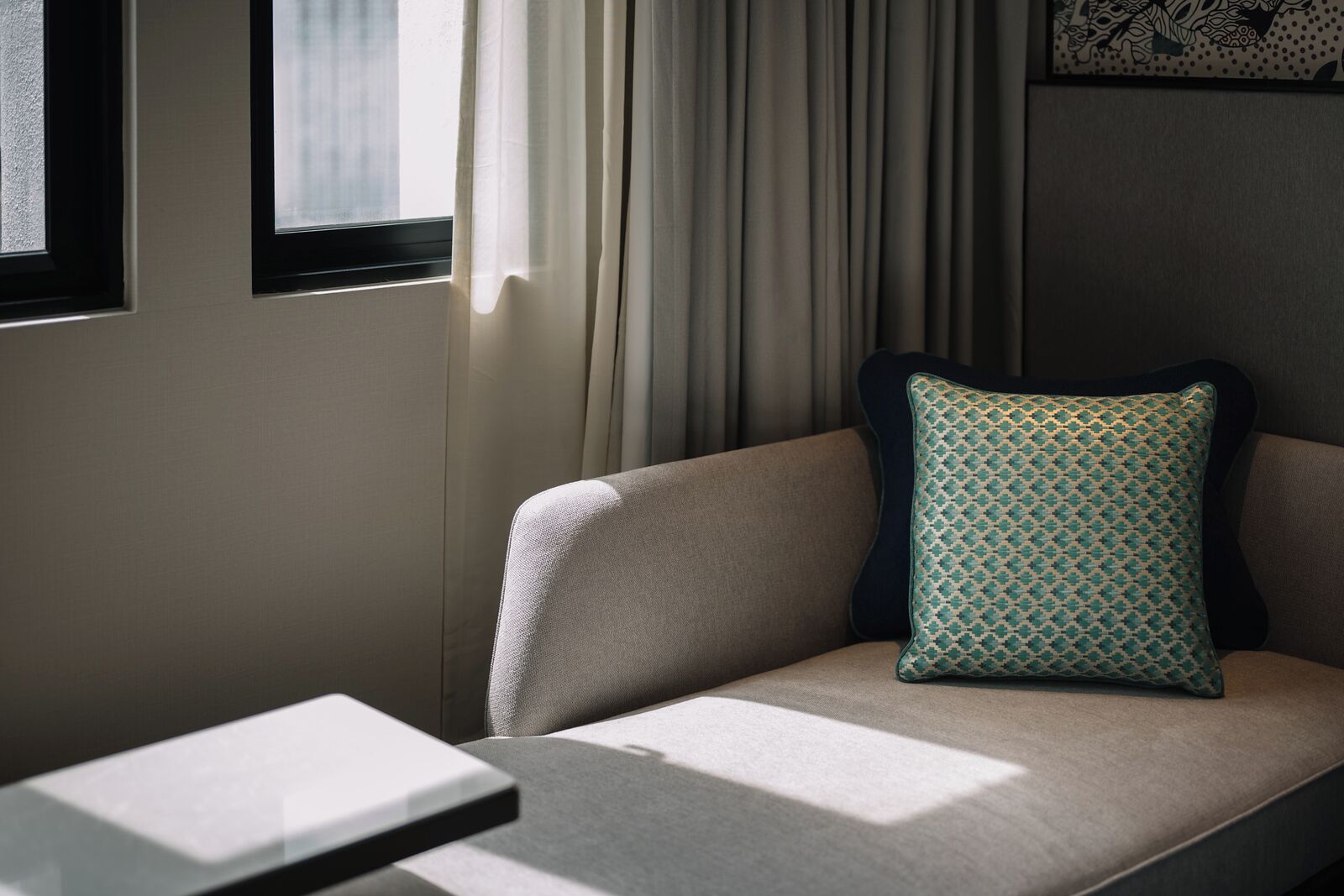 Ein modernes Hotelzimmer mit einer Couch, einem gemusterten Kissen und einem Fenster mit Vorhängen.