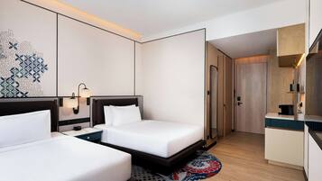 Una camera d'albergo con due letti, una scrivania, uno specchio e l'ingresso del bagno.