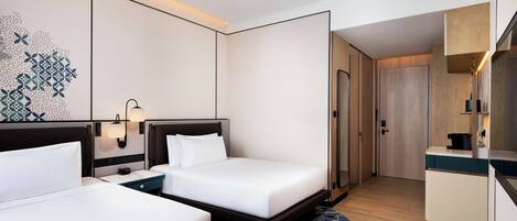 A hotel room with two beds, a desk, a mirror, and a bathroom door.