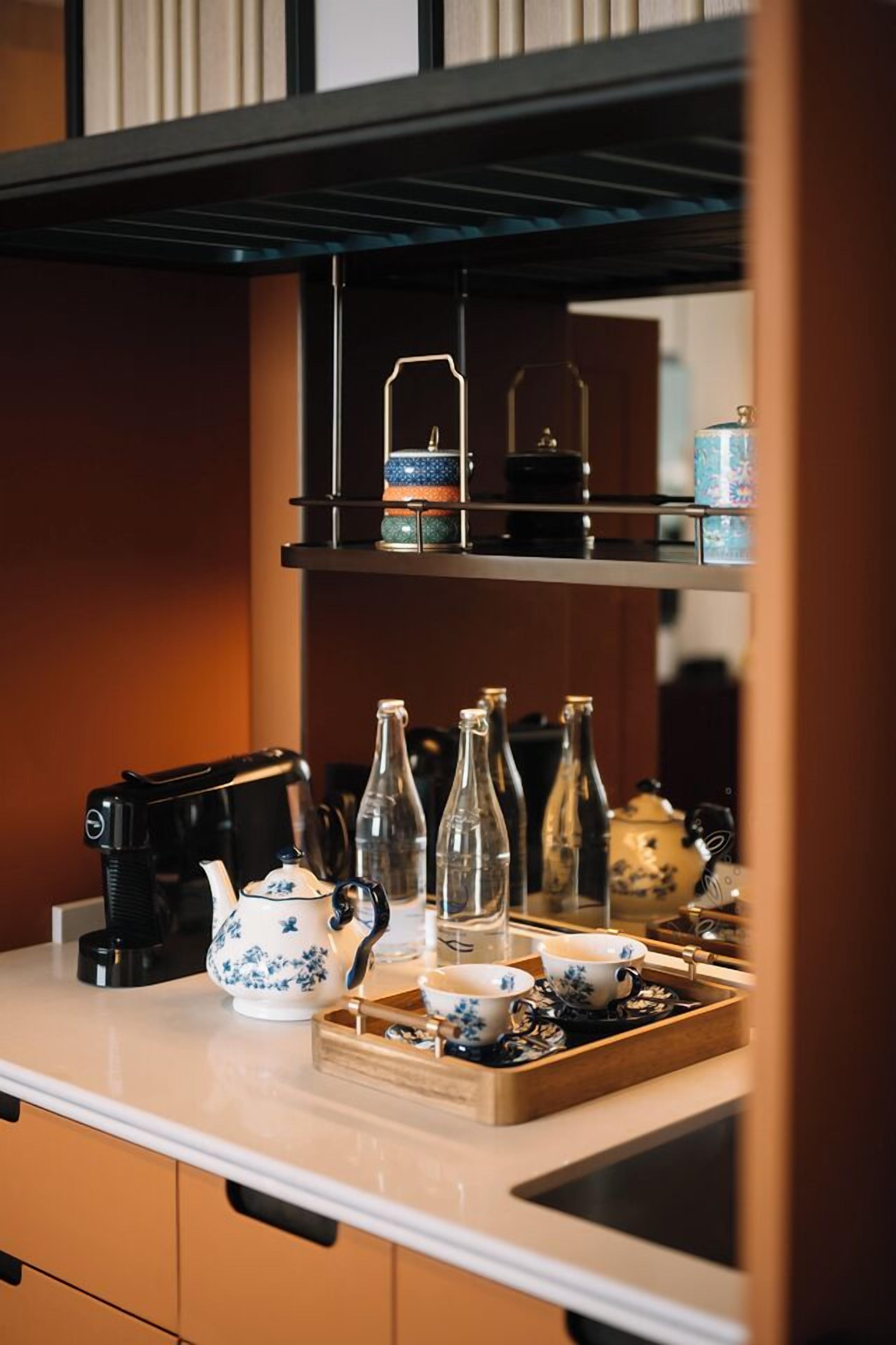 A kitchen counter with a coffee maker, teapot, cups, and bottles.