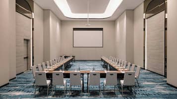 A conference room with a long table and chairs, a projector screen, and a carpeted floor.