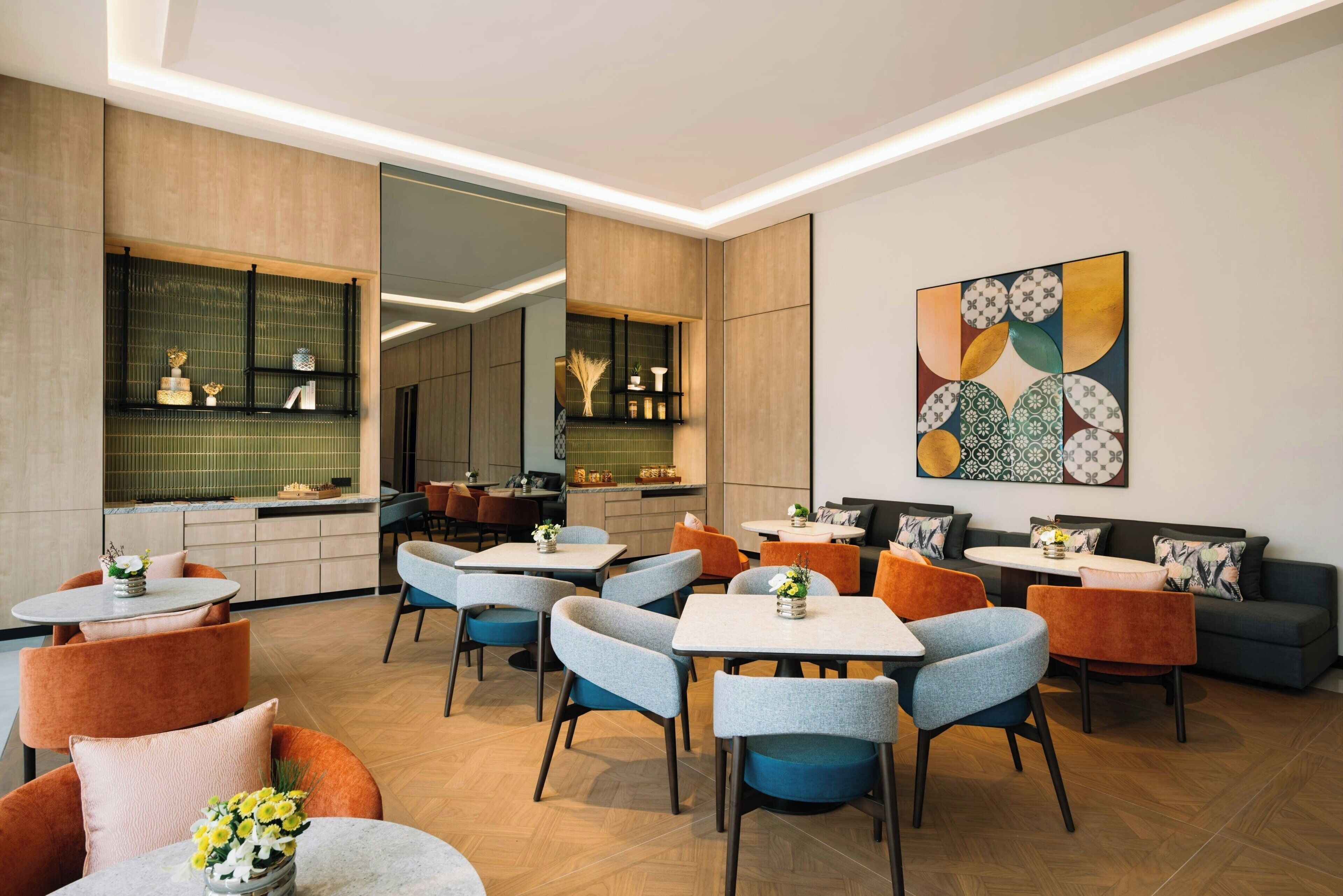 A modern dining area with multiple tables and chairs, a kitchen in the background, and a decorative wall piece.