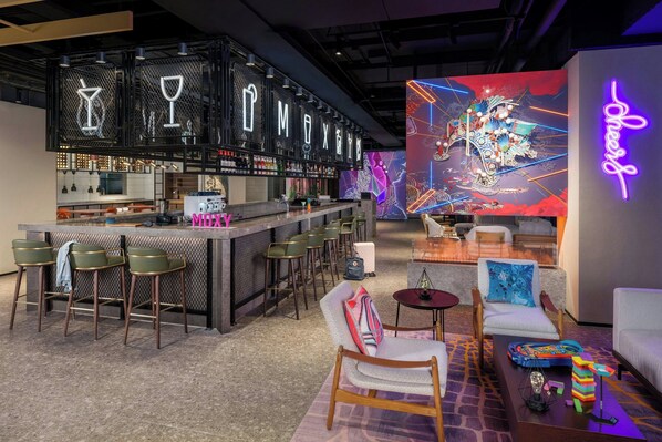 A bar area with a neon sign, bar stools, and a seating area with a colorful mural. - Moxy Suzhou City Centre (Suzhou)