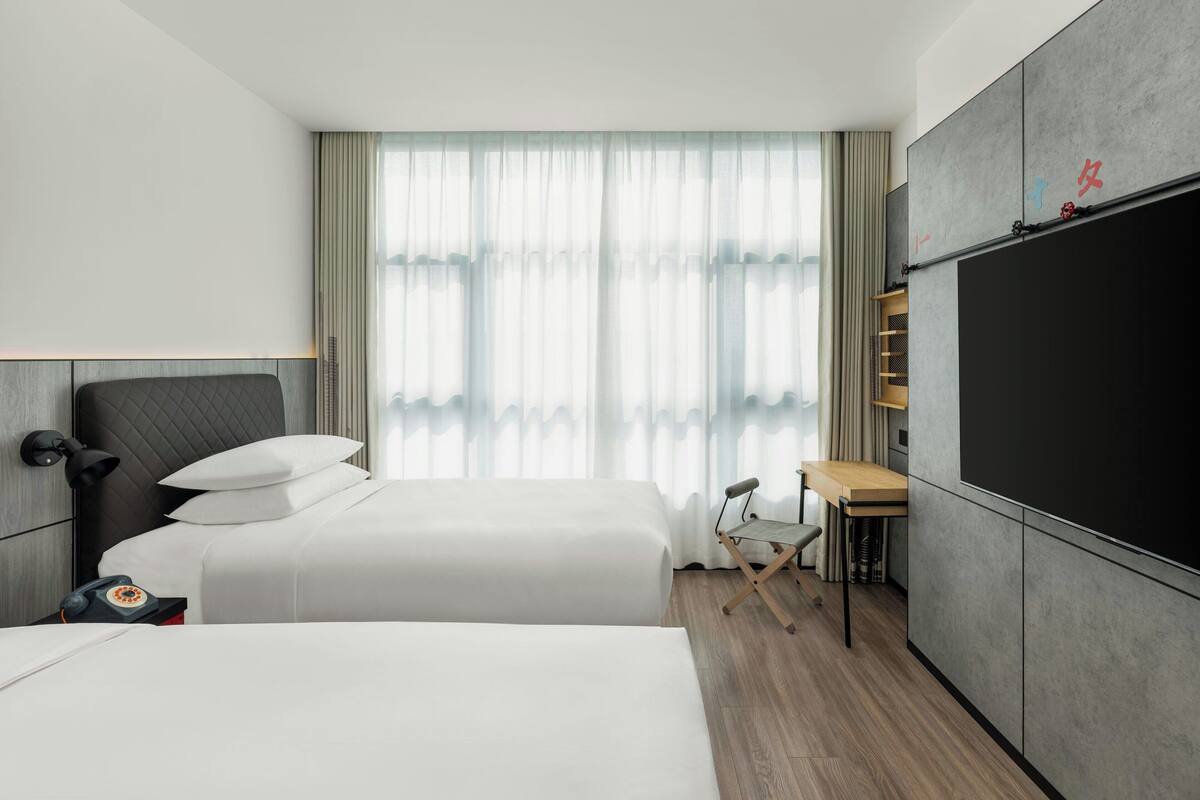 A hotel room with two beds, a desk, a chair, a TV, and a wardrobe.