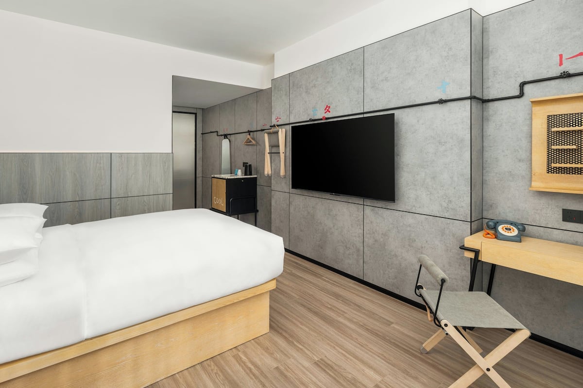 A modern bedroom with a bed, a desk, and a TV mounted on the wall.