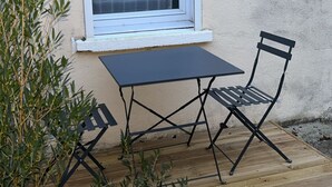 En uteplats med ett bord och två stolar, ett fönster och en krukväxt.
