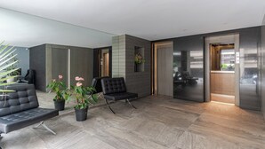 Un vestíbul modern amb un sofà de cuir negre, una cadira negra i plantes en testos.