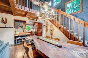 Un'ampia sala da pranzo con un grande tavolo in legno, un lampadario e una scala con ringhiere in legno.