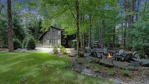 Una cabaña con un hogar de piedra y mobiliario exterior, rodeada de un paisaje boscoso.