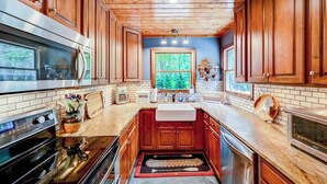 Una cocina con armarios de madera, un horno de acero inoxidable, un fregadero y una ventana con vistas a árboles.