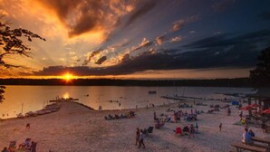 Una playa con un atardecer, barcos y gente relajándose.