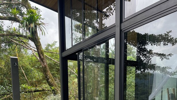 Un espace extérieur moderne, aménagé avec deux chaises en bois et une table en verre, entouré de plantes en pot et offrant une vue sur une végétation luxuriante.