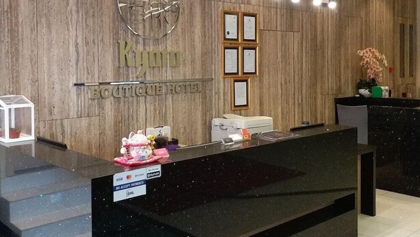 Un comptoir d’accueil d’hôtel avec un mur en bois en arrière-plan, des certificats encadrés et une horloge.