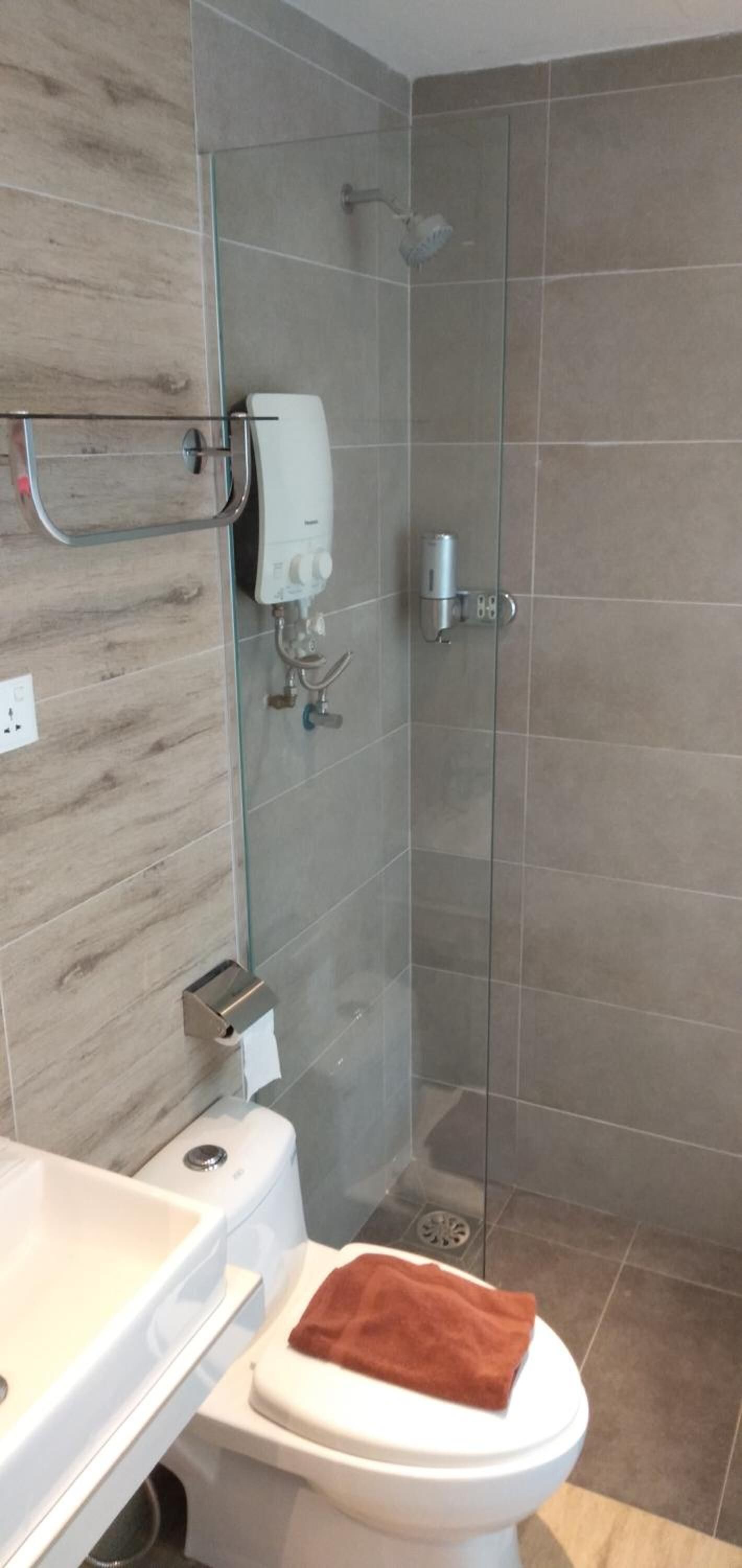 A modern bathroom with a glass shower enclosure, a white toilet, and a beige tiled wall.