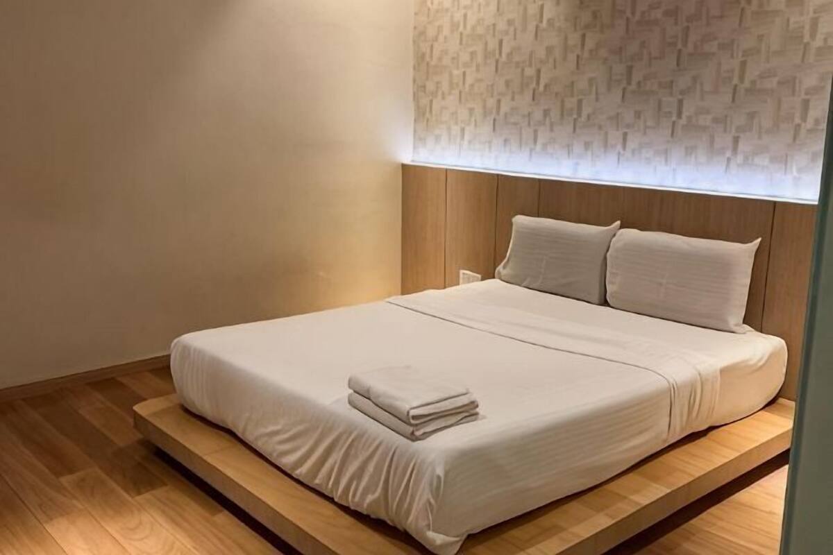 Un lit bien fait, recouvert d’une couvre-lit blanche et agrémenté d’oreillers, une structure en bois sous le lit et un mur décoré d’un motif.