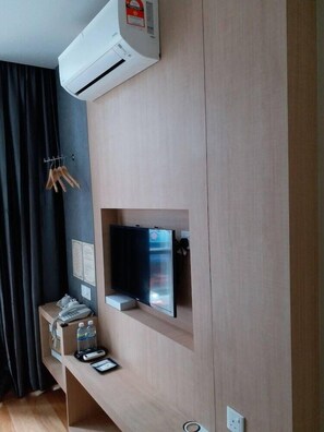 Une chambre moderne équipée d’un téléviseur encastré, d’une petite étagère avec un téléphone et une bouteille d’eau, et d’un climatiseur fixé au mur.