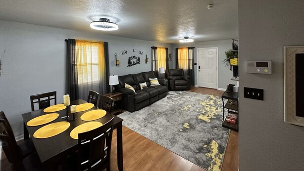 A living room with a black leather sofa, a dining table with yellow placemats, and a grey rug with yellow accents. - Cute 3 bedroom, 1 bath home less than 5 minutes from downtown. (Hot Springs)