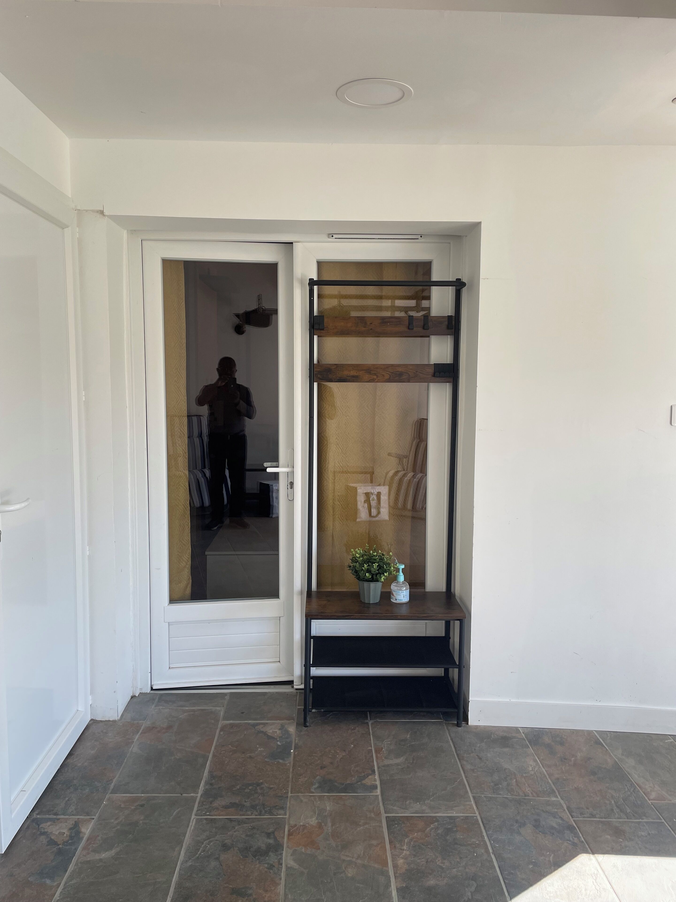A hallway with a door leading to a room. A small bench with a potted plant and a bottle is placed against the wall.
