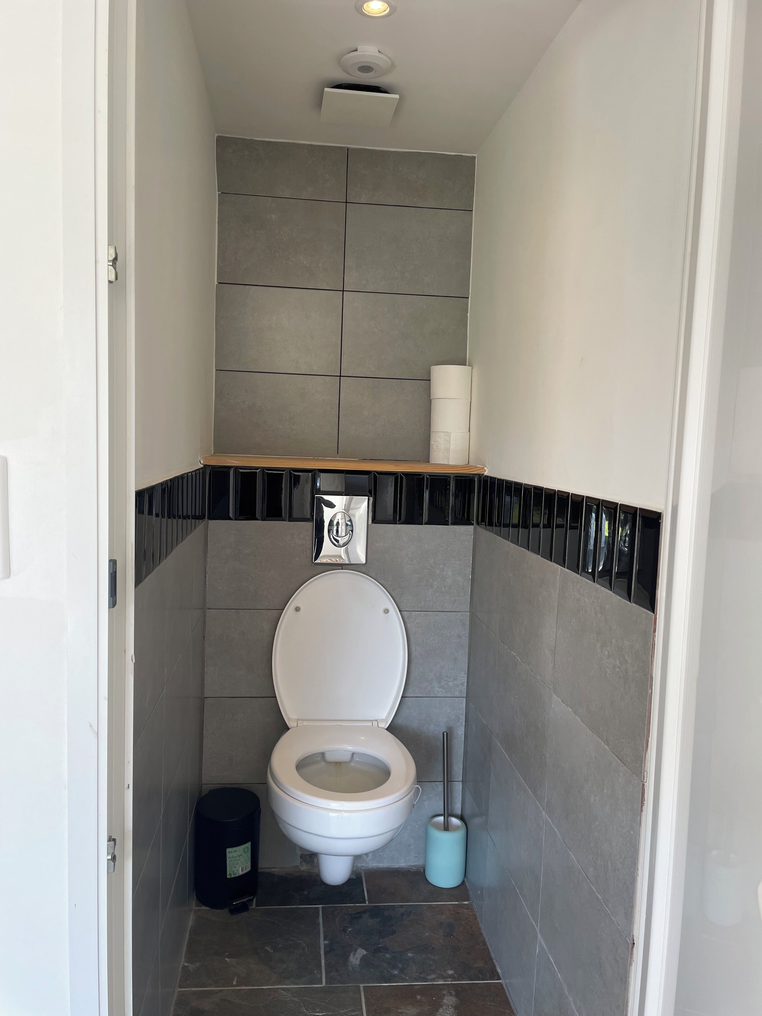 Une petite salle de bain comprenant des toilettes, une poubelle et une brosse à récurer les toilettes.